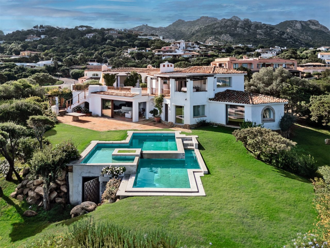 Vista aerea di una villa con giardino e piscina in primo piano. Sullo sfondo le colline e i monti attorno Porto Cervo e altre ville.